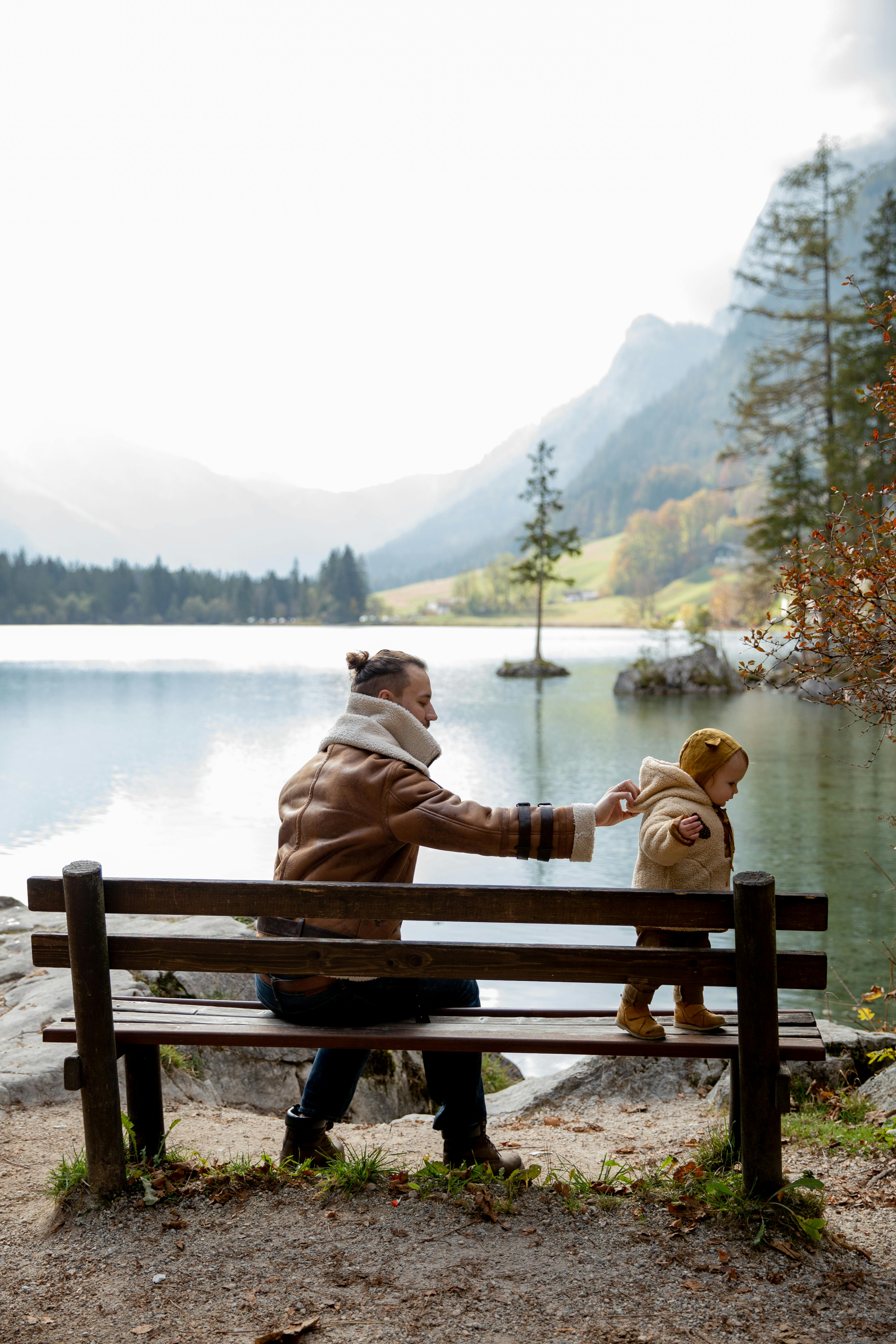 Vater hält sein Kleinkind beim Stehen auf einer Holzbank am Bergsee