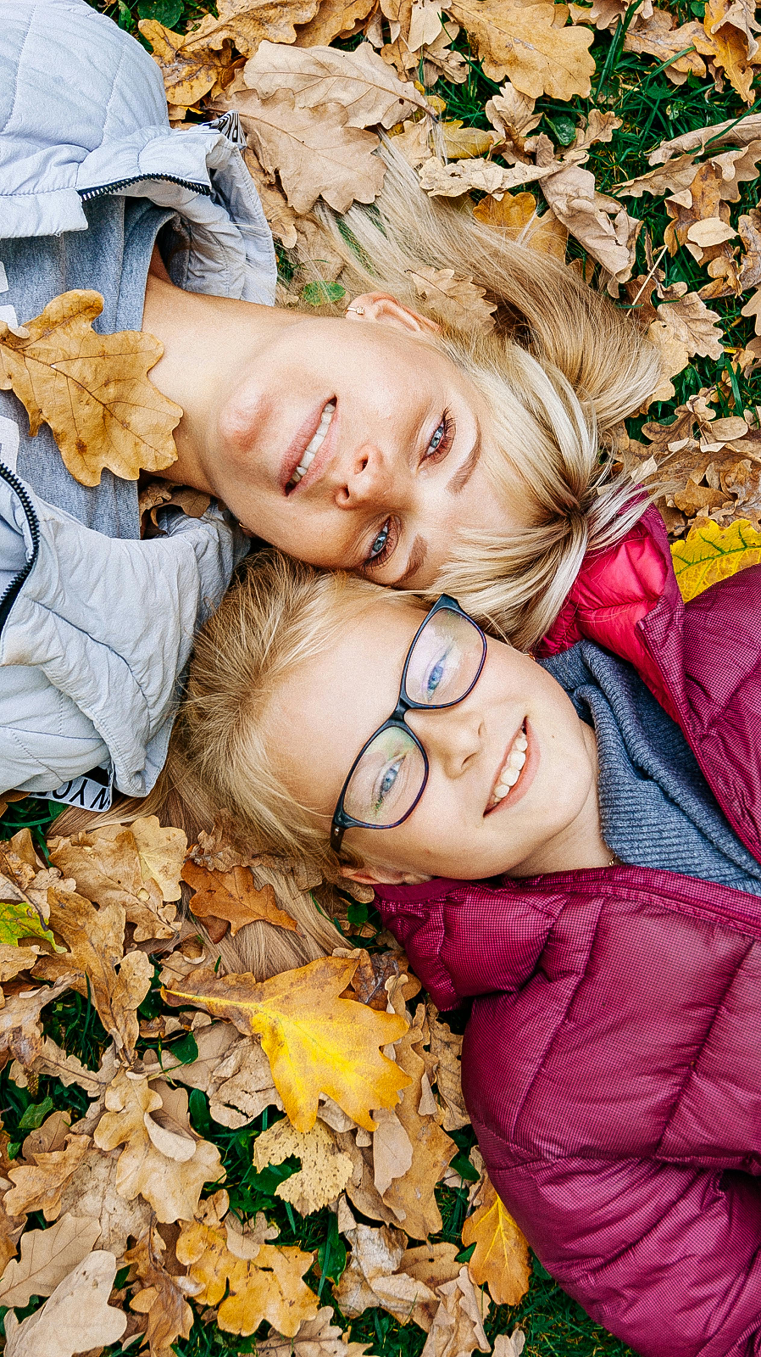 Mutter und Tochter liegen lachend im Herbstlaub